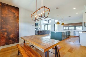 Una cucina moderna con tavolo da pranzo in legno, lampade a sospensione e un'ampia finestra che permette l'ingresso di luce naturale.