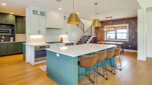 A modern kitchen with a central island, bar stools, and a staircase leading to another level. - Nat'l Forest Access & Mtn Views: Family Eagar Home (Eagar)