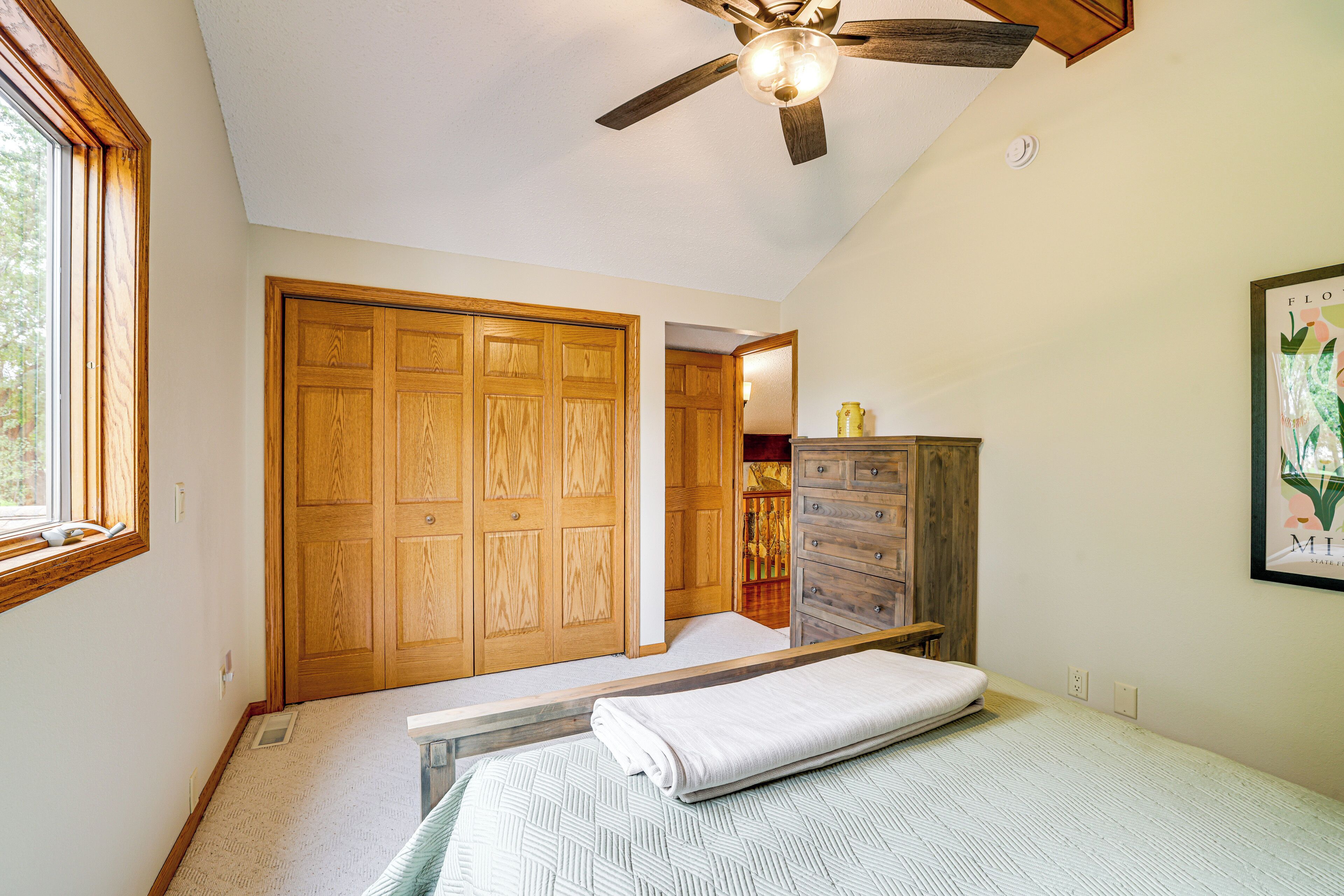 A bedroom with a bed, wooden wardrobe, ceiling fan, and a window.