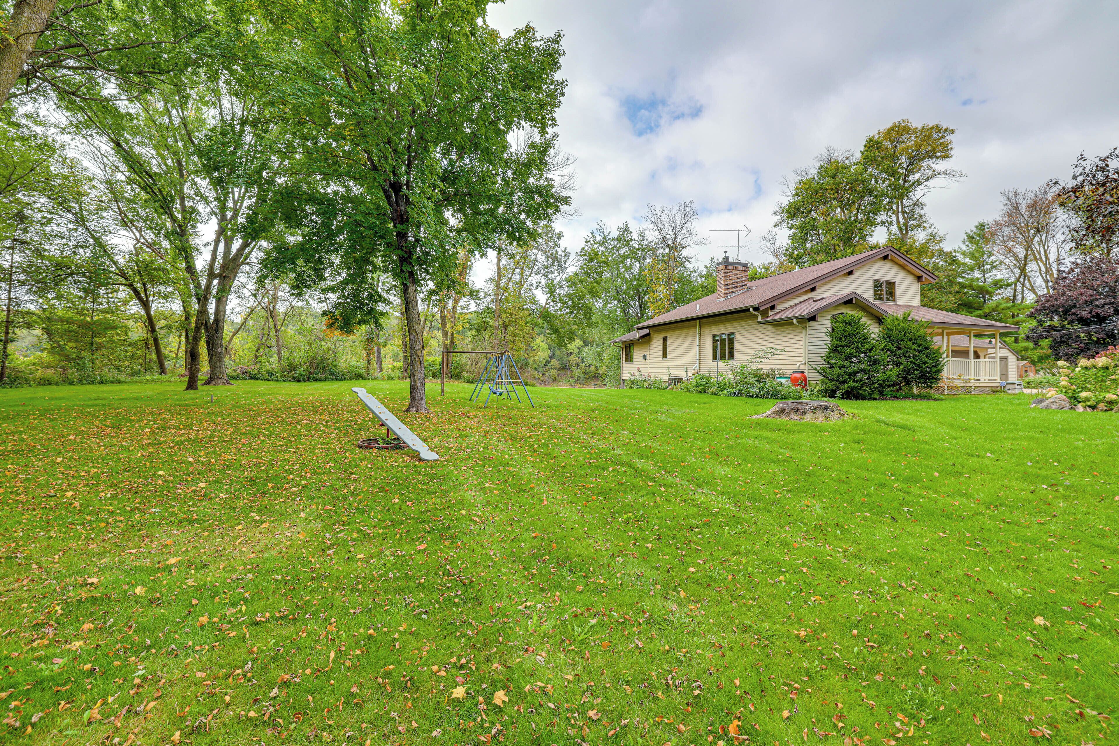 A house with a well-maintained lawn, a swing set, and a large tree in the foreground.