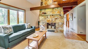 A spacious living room with a stone fireplace, a wooden ceiling, and a large window overlooking a garden. - Mississippi River Home 8 Mi to Dtwn St Cloud! (St Cloud)