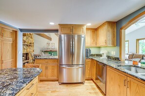 Una cocina con armarios de madera, un refrigerador de acero inoxidable, encimeras de granito y un lavavajillas.