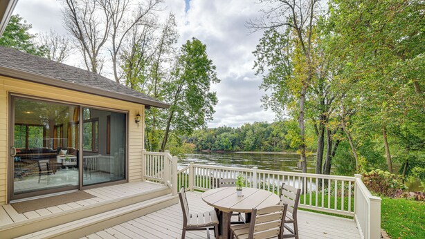 A wooden deck with a glass door leading to a covered area, a round table with chairs, and a view of a lake surrounded by trees. - Mississippi River Home 8 Mi to Dtwn St Cloud! (St Cloud)