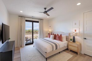 Ein Schlafzimmer mit einem Bett, einem Fernseher, einem Deckenventilator, einem Nachttisch mit Lampe und einer Schiebeglasdoor zum Balkon.