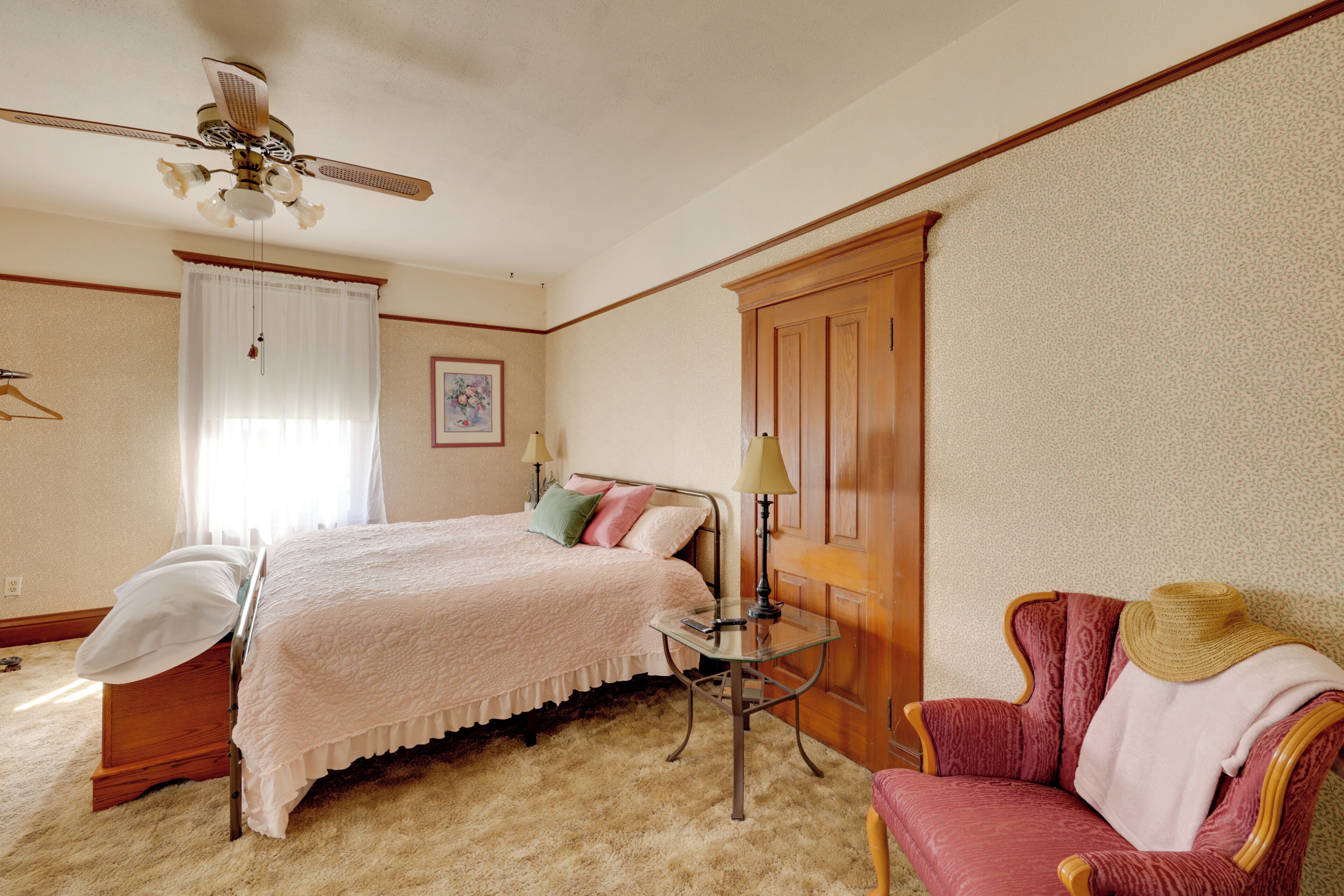 Un dormitorio con una cama, una silla, una mesa, un ventilador de techo y una puerta.