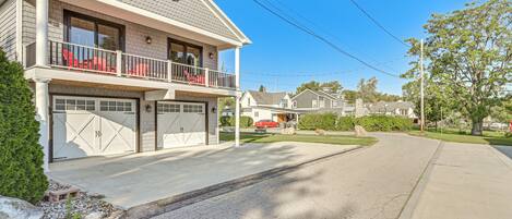 Une maison à deux étages avec un garage, un balcon orné de chaises rouges et une voiture rouge garée dans l’allée.