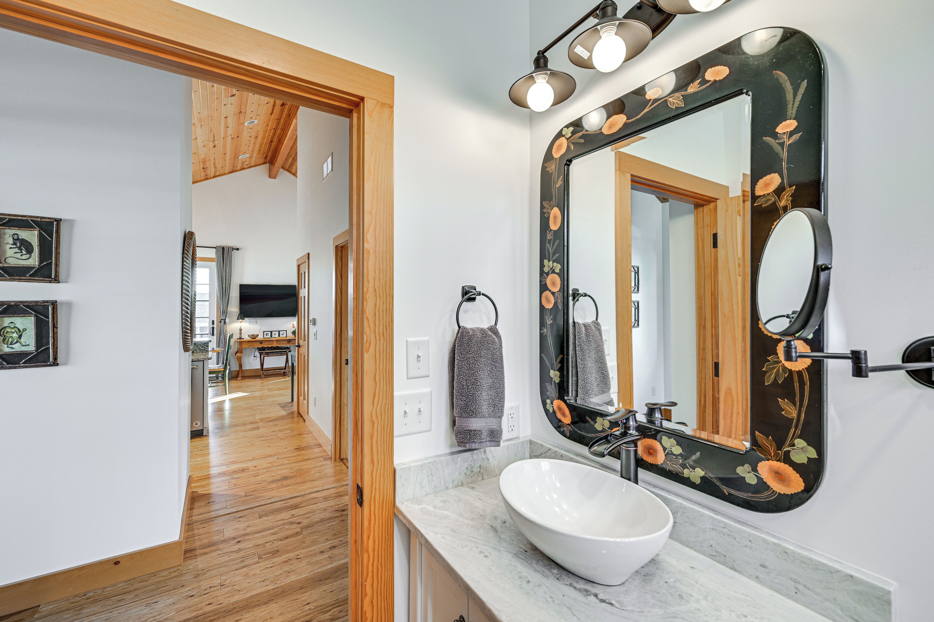 A bathroom with a white sink, a large mirror with floral design, and wooden flooring.