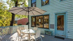 A covered outdoor seating area with a table and chairs, a large umbrella, and a view of a house with a blue door and windows. - 4 Mi to Dtwn Loveland: Private Retreat w/ Decks (Loveland)