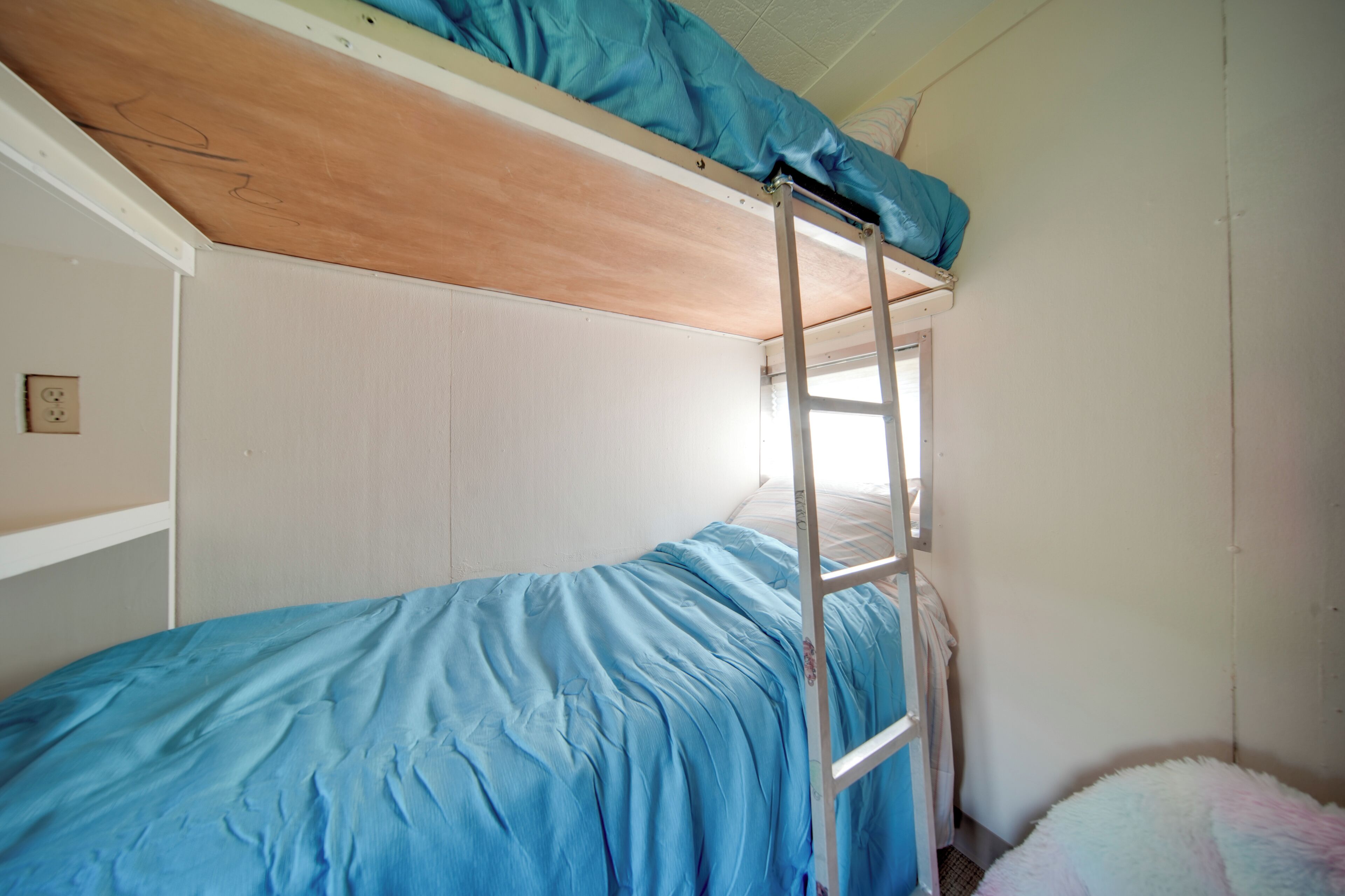 Una cama litera con escalera, una ventana y un almohadón mullido.