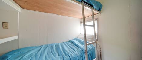 Una cama litera con escalera, una ventana y un almohadón mullido.