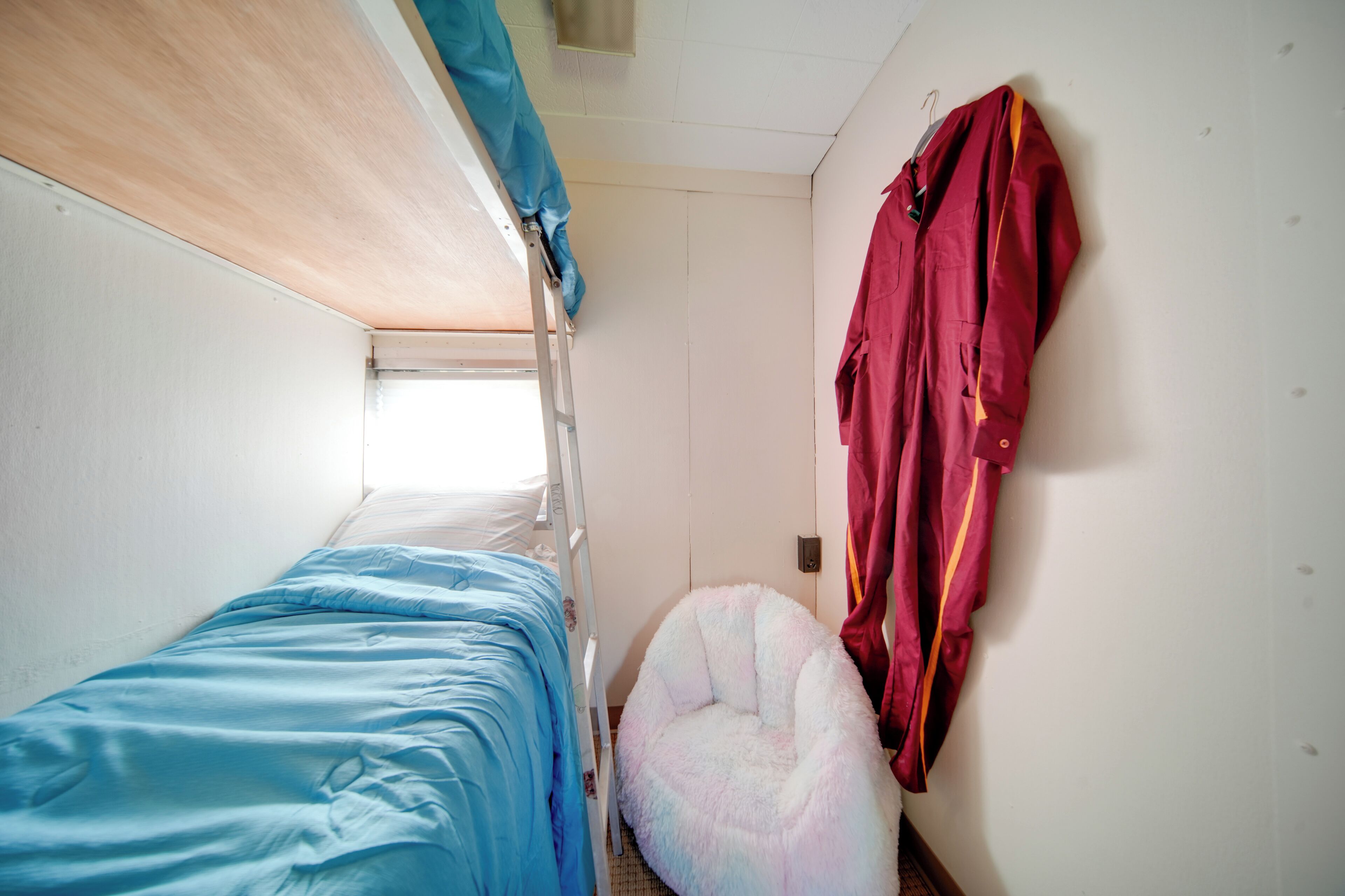 Ein Etagenbett mit blauer Matratze, ein flauschiger Sitzsack und eine rote Jacke, die an der Wand hängt.