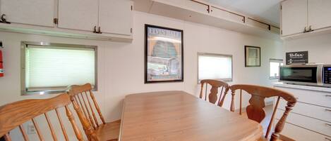 A dining area with a wooden table and chairs, a framed picture on the wall, and a microwave in the background.