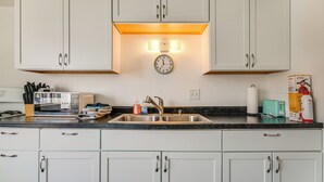 Une cuisine avec des meubles blancs, un four à micro-ondes, un évier et une horloge au-dessus de l’évier.