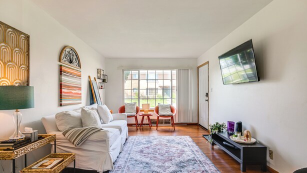 Un salon moderne avec un canapé, des fauteuils, une table basse, un téléviseur et des œuvres d’art accrochées aux murs.