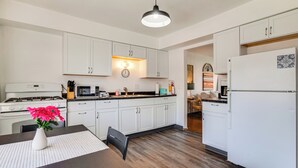 Une cuisine moderne avec des meubles blancs, un plancher en bois, une table à manger ornée d’un vase de fleurs et un réfrigérateur.