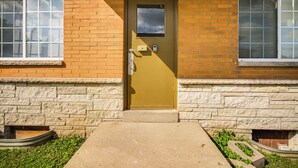 Une porte jaune avec une petite fenêtre au-dessus, une boîte aux lettres et un marchepied en béton menant à la porte.