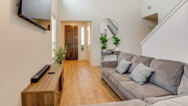 A modern living room with a wooden coffee table, a grey sofa with patterned cushions, a mounted flat-screen TV, and a staircase leading to an upper level. - Yard & Office: Spacious Family Home in Forney (Forney)