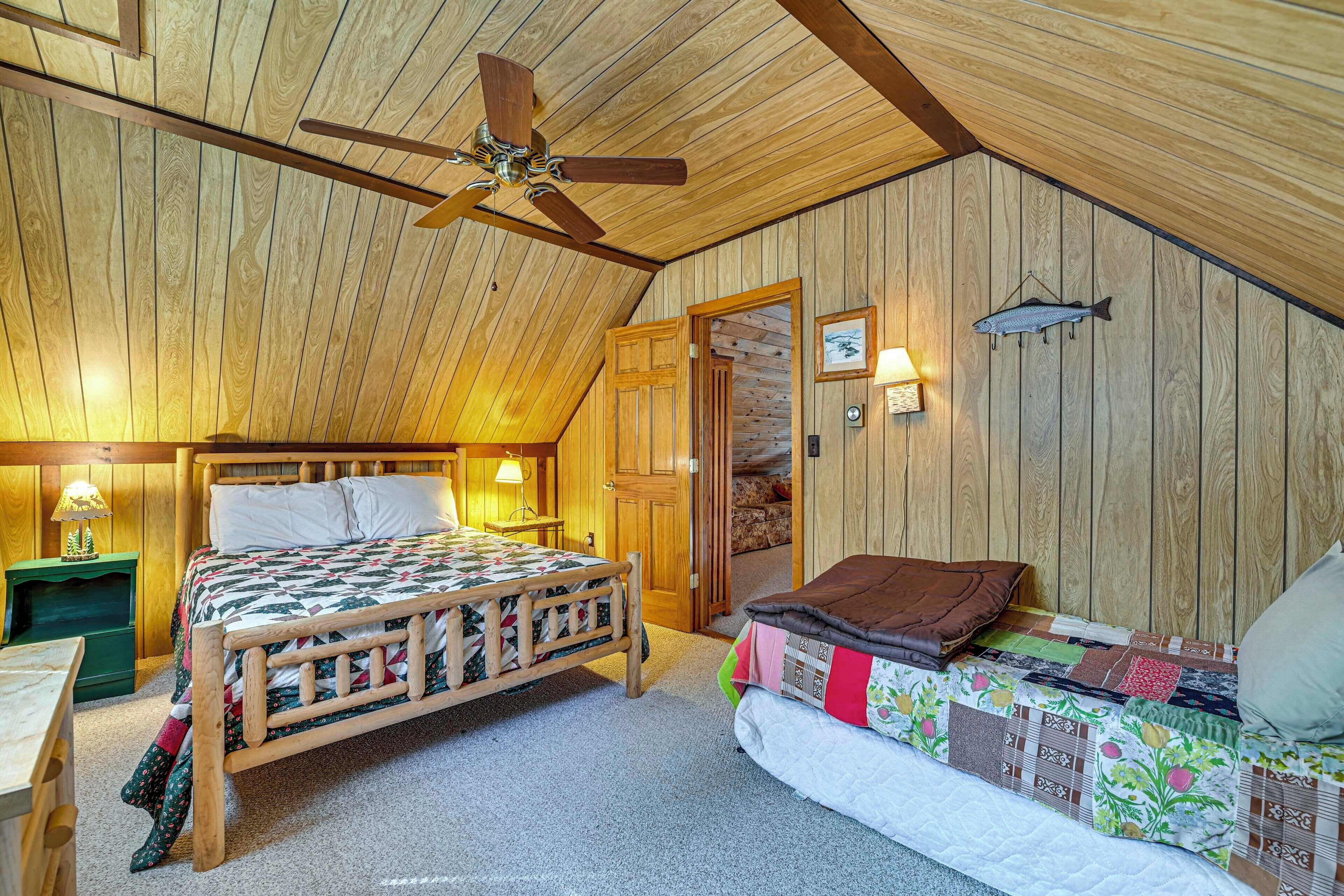 A cozy bedroom with a wooden ceiling, a bed with a quilt, a sofa with a blanket, a wall-mounted fish, and a door leading to another room.