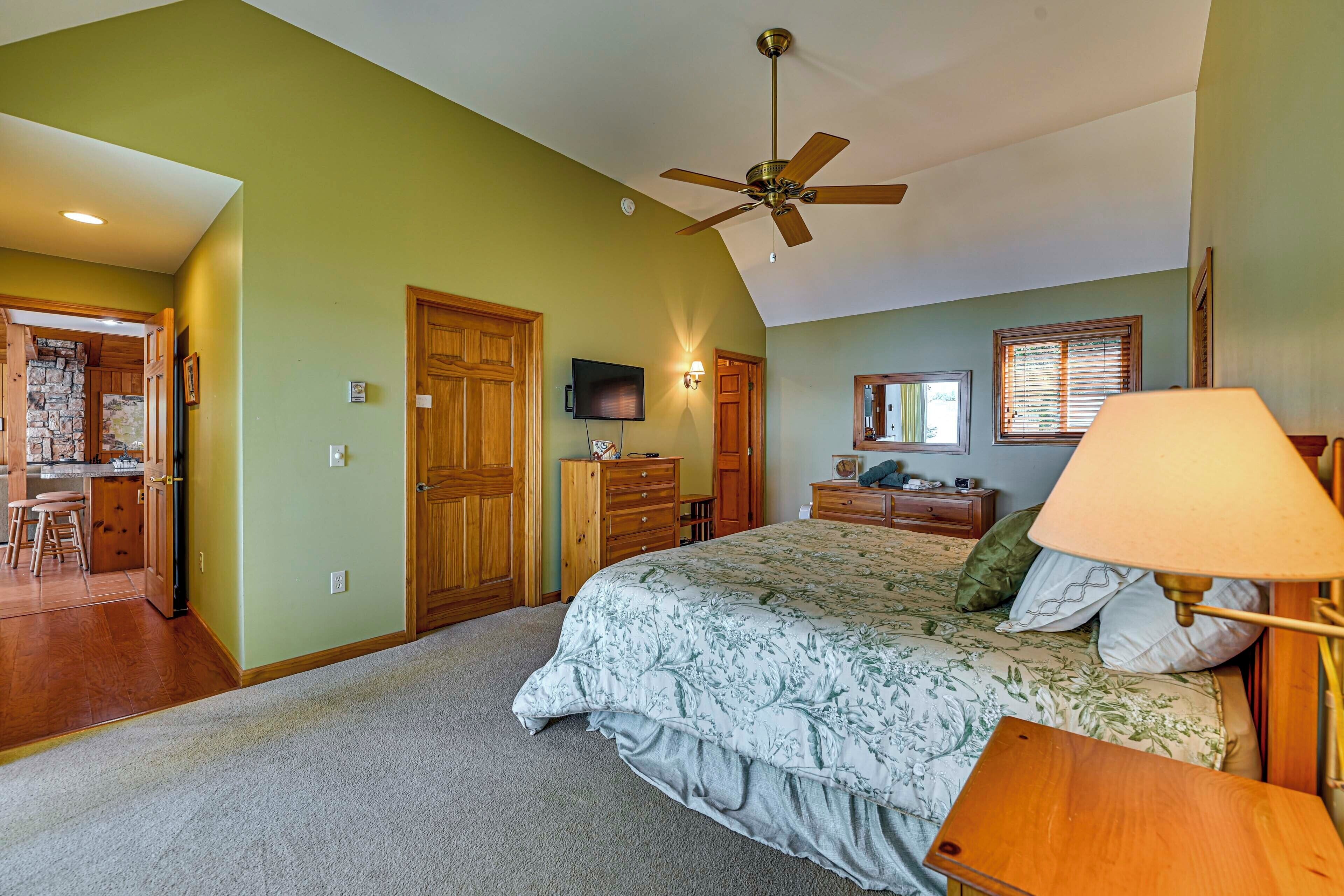 A bedroom with a bed, a ceiling fan, a TV, and a wooden dresser.