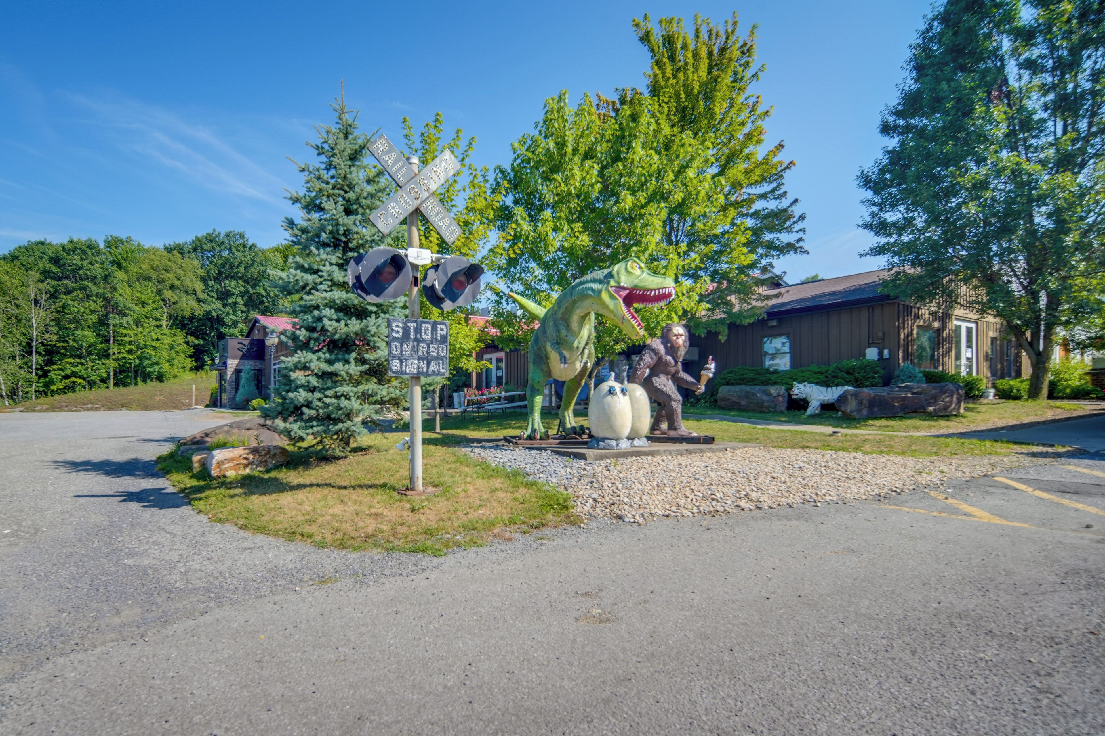 A road intersection with a railroad crossing sign, a dinosaur statue, and a lion statue.
