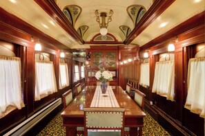 A dining car with a long table, chairs, and a vase with flowers. - The Presidential Stay, Converted Railcar in Dubois (DuBois)