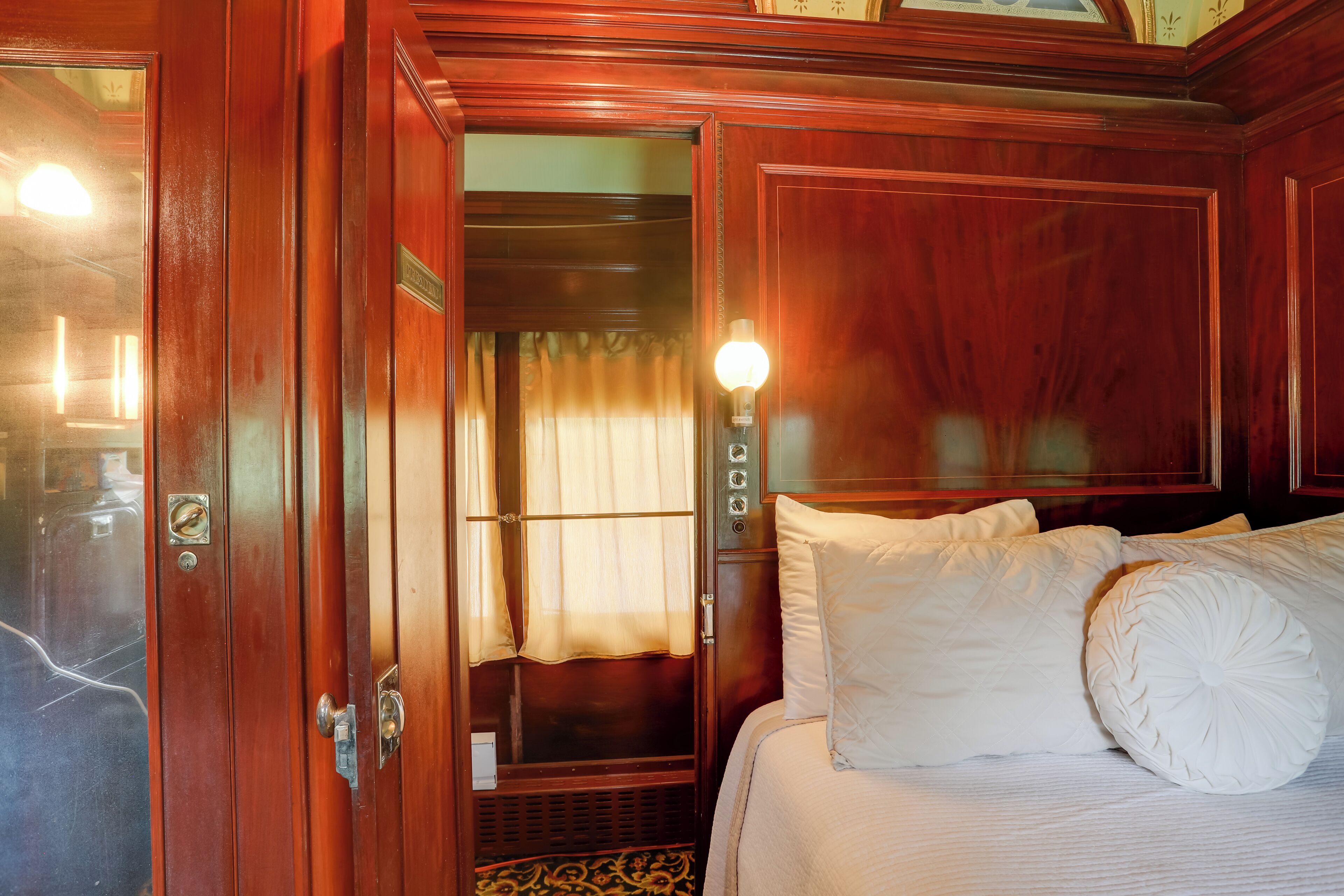 Une pièce en bois avec un lit, une porte donnant sur une salle de bain et un luminaire fixé au mur.