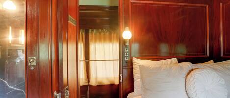 A wooden room with a bed, a door leading to a bathroom, and a wall-mounted light fixture.