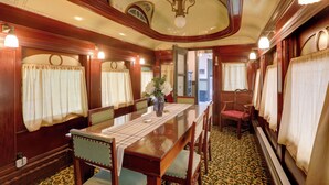 A dining car with wooden furniture, a central table, and curtains on the windows.