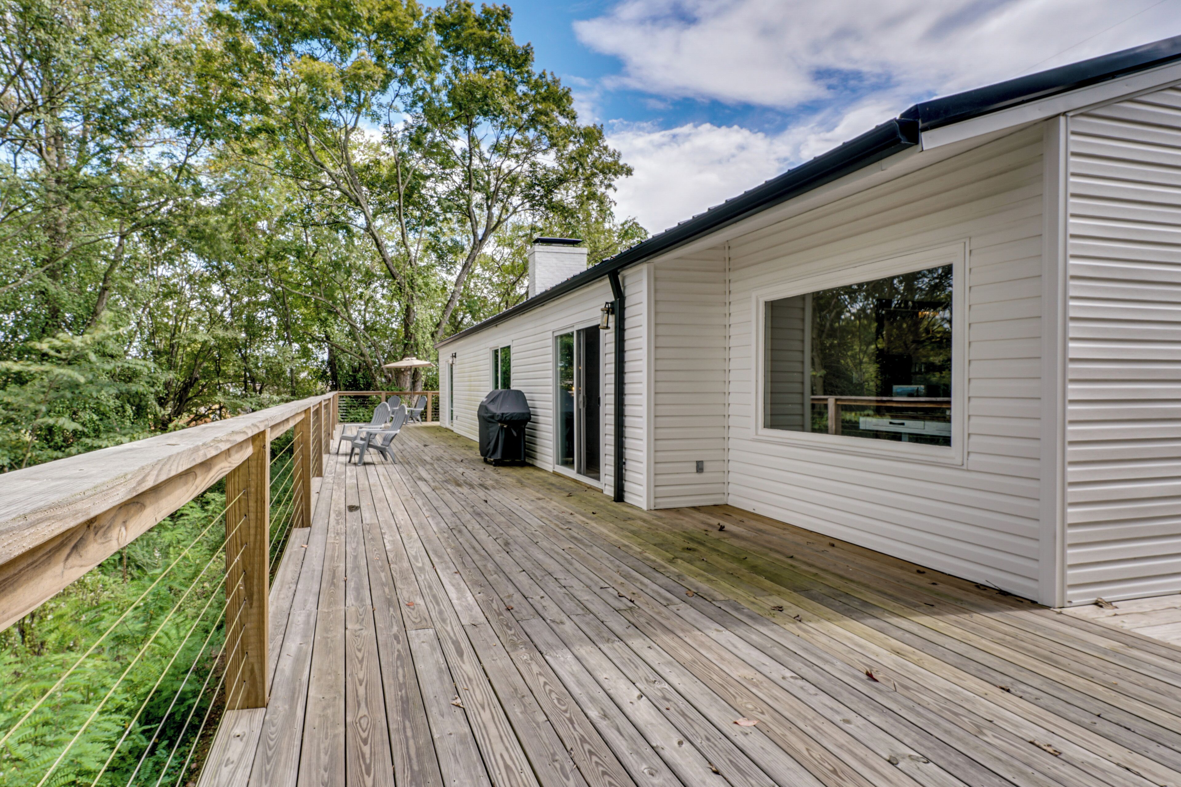 A wooden deck with a railing, a covered outdoor seating area, and a white building with windows and a door.