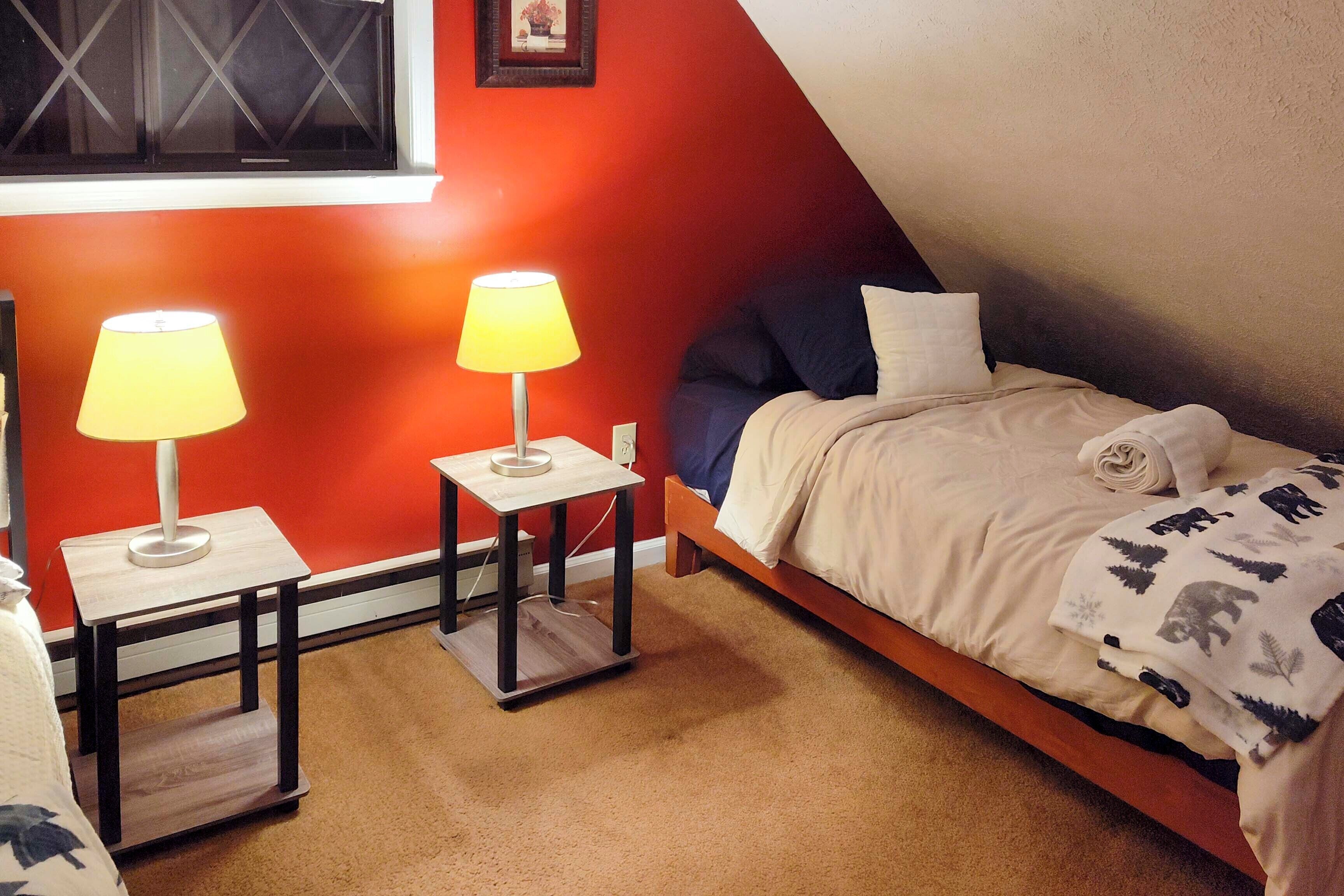 Une chambre à coucher avec un lit, deux tables de chevet avec des lampes, une fenêtre et un mur rouge.