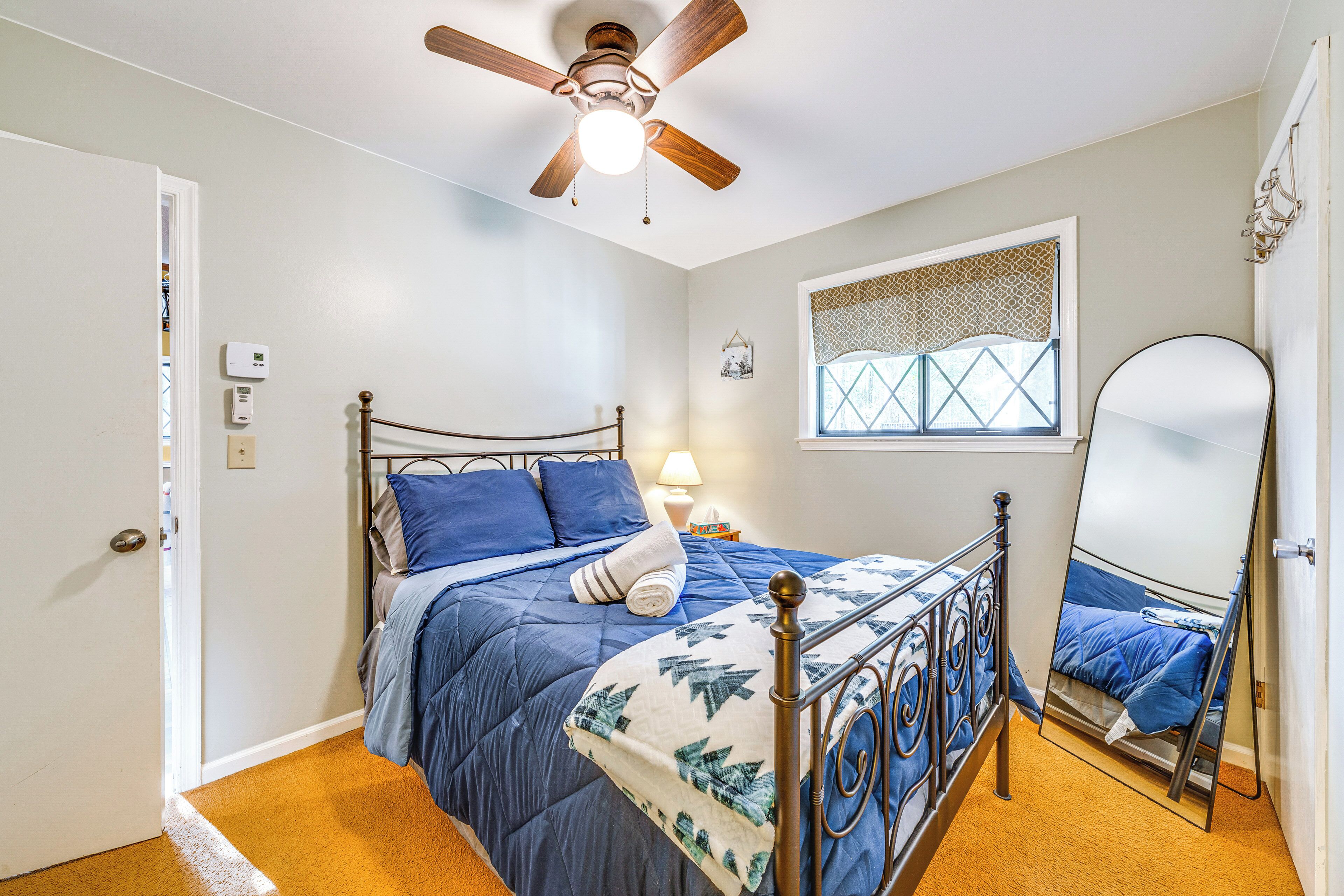 Un dormitorio con cama, ventilador de techo, ventana con celosía decorativa y espejo.