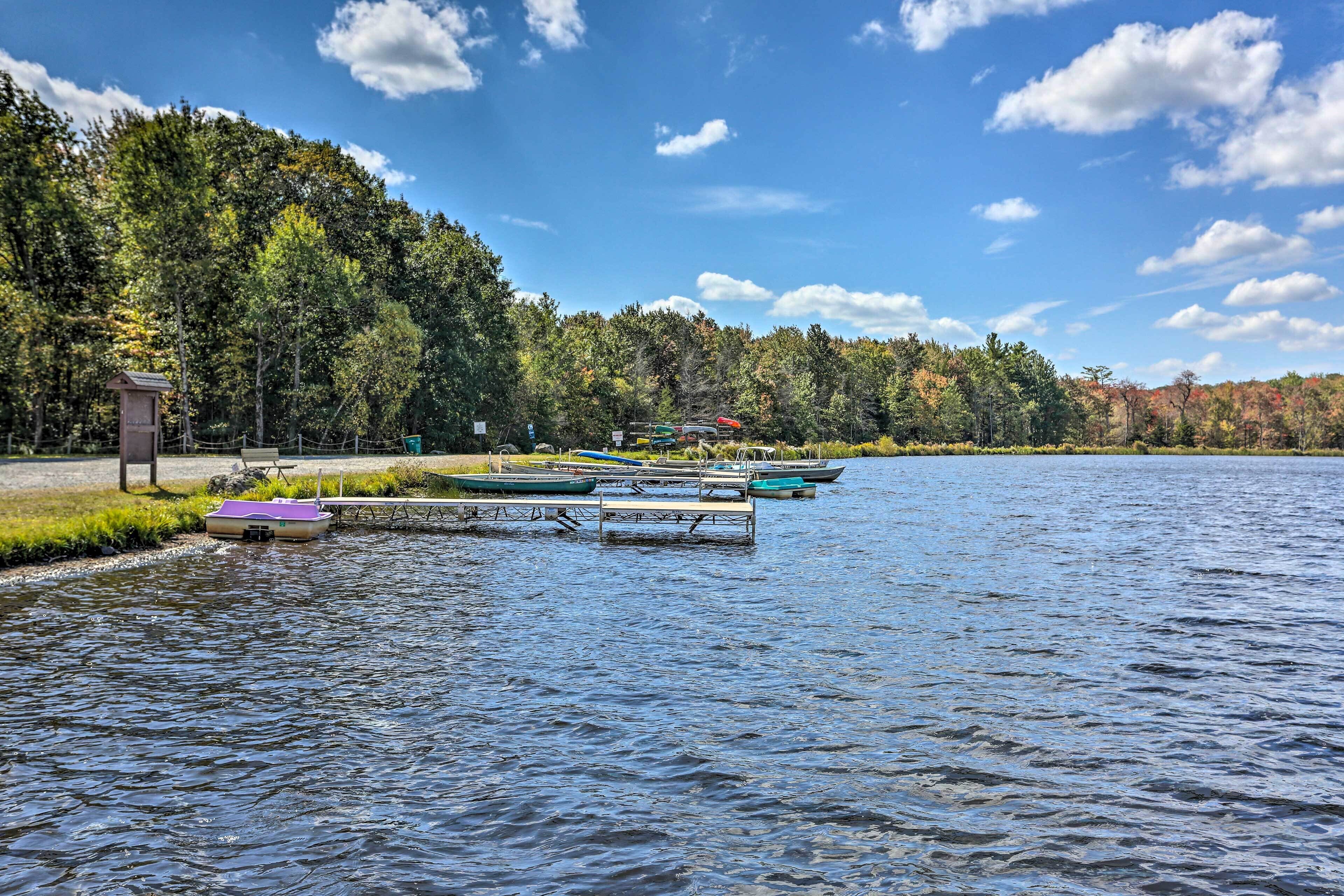 A lakeside view with docked boats, a picnic area, and a forested shoreline.