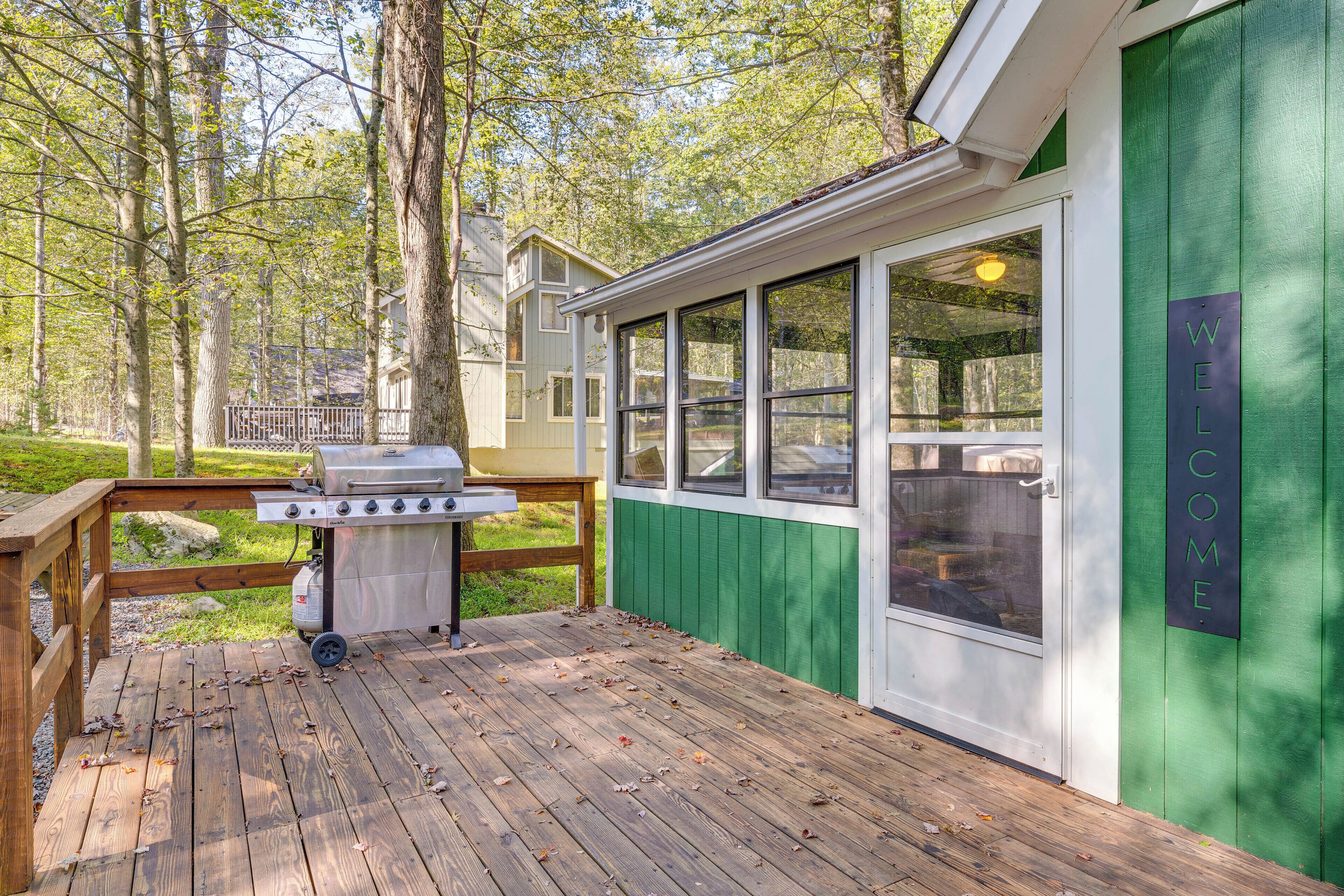 Une terrasse avec un barbecue, un mur extérieur vert et une fenêtre ornée d’une pancarte « BIENVENUE ».
