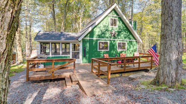 A cabin with a green exterior, a porch with wooden benches, and an American flag. - Featured on Hgtv! Visit This Lottery Dream Home! (Pocono Lake)