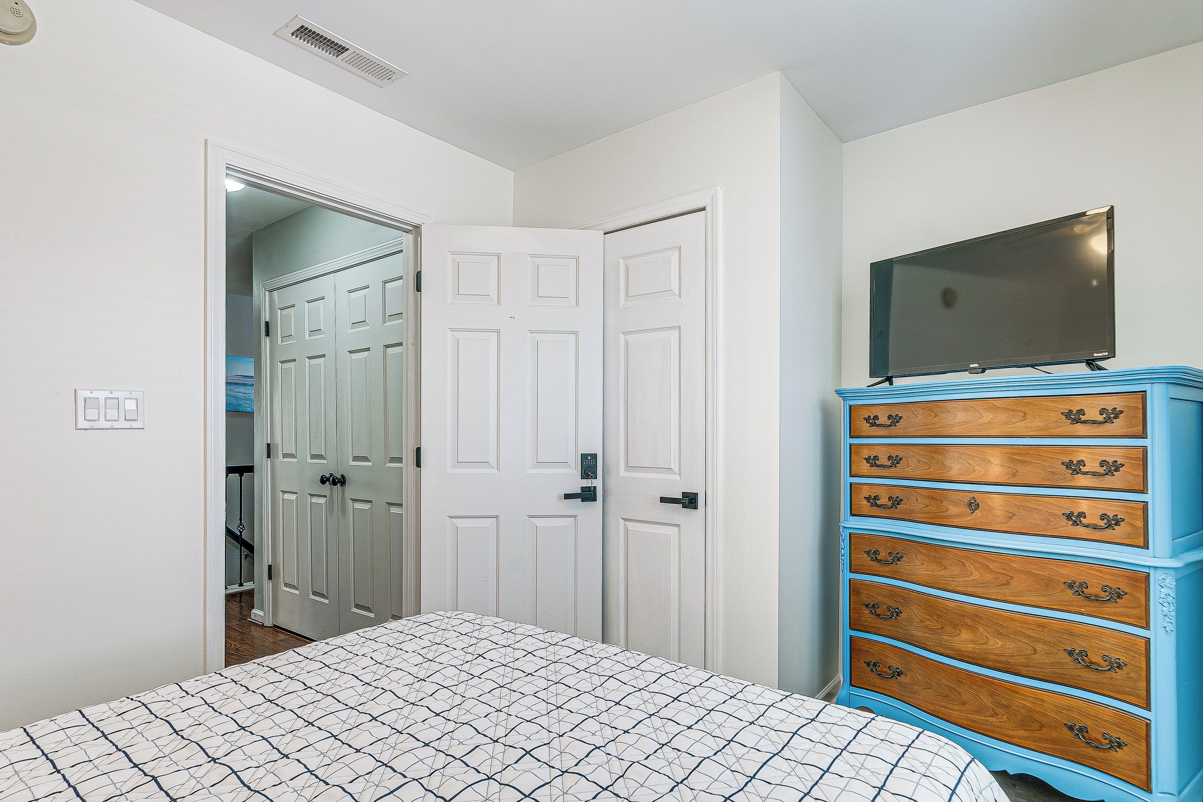A bedroom with a bed, a dresser, and a TV on the wall.