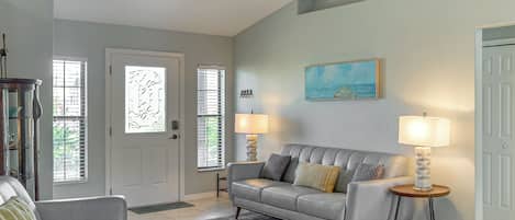 Een woonkamer met een grijze bank, twee bijzettafels met lampen, een grijs vloerkleed en een schilderij aan de muur.
