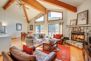 A spacious living room with a stone fireplace, leather sofas, and a large window overlooking a forested area. - < 1 Mi to Diamond Peak: Townhome w/ Lake Views (Incline Village)