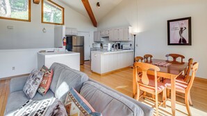 A spacious living area with a gray sofa, wooden dining table, and chairs, a kitchen with white cabinets, and a large window overlooking greenery. - < 1 Mi to Diamond Peak: Townhome w/ Lake Views (Incline Village)