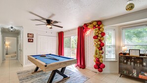 A pool table in a room with a ceiling fan, a cabinet with glass doors, and a view of the outdoors through windows. - Walk to Campus, FSU Photo Wall: Inviting Retreat! (Tallahassee)