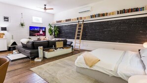 Een moderne woonkamer met een prikbord, boekenkasten, een televisie en een gezellige zithoek.