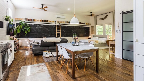 Una cocina moderna con suelo de madera, un comedor con mesa de mármol y una sala de estar acogedora con sofá y chimenea.