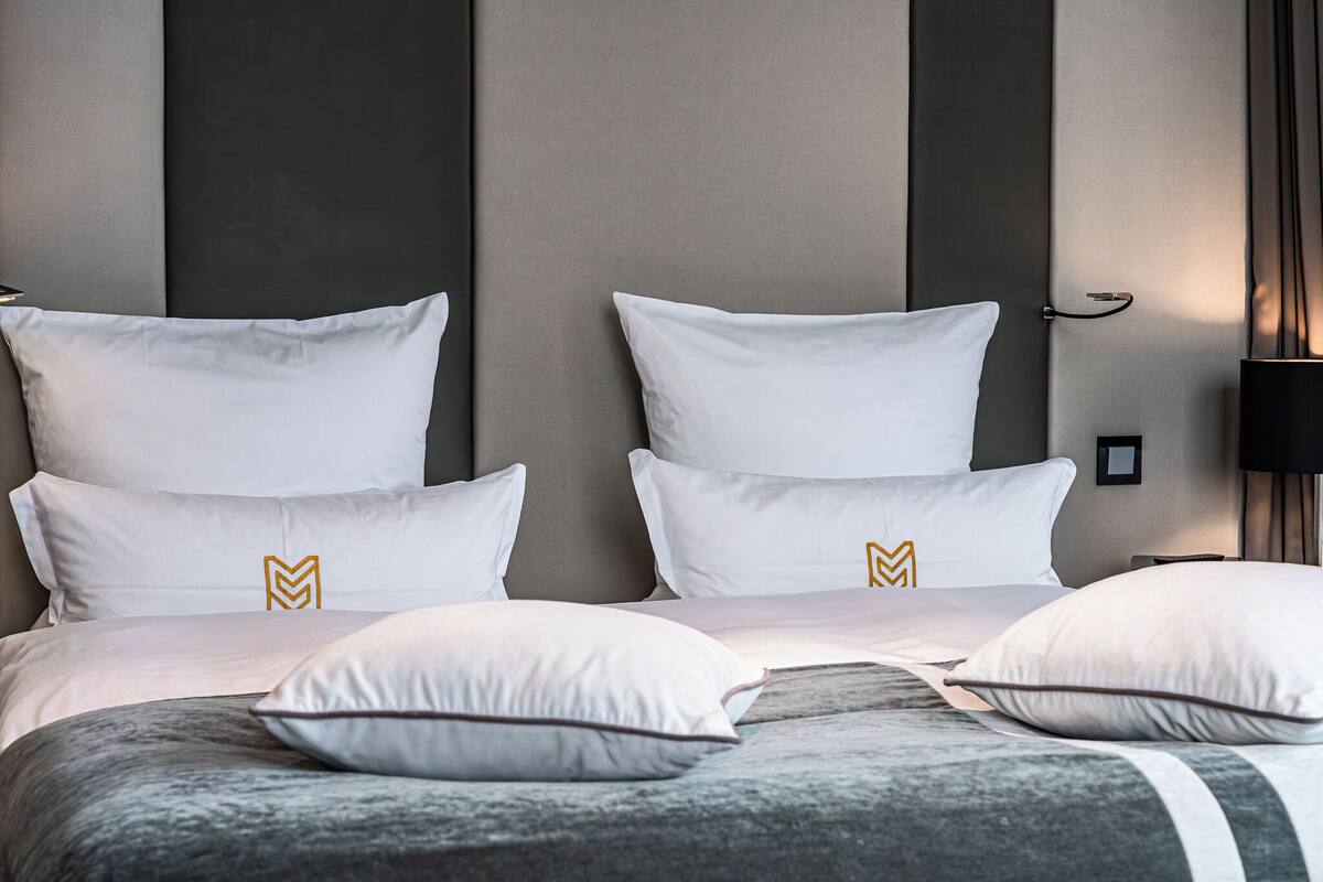 A neatly made bed with white bedding and a grey headboard.