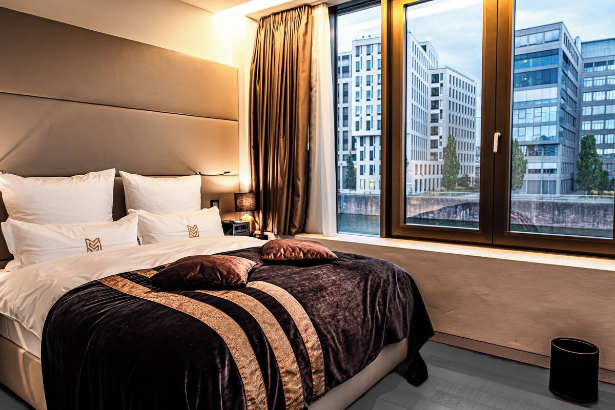 A modern hotel room with a large bed, city view, and a window with curtains.