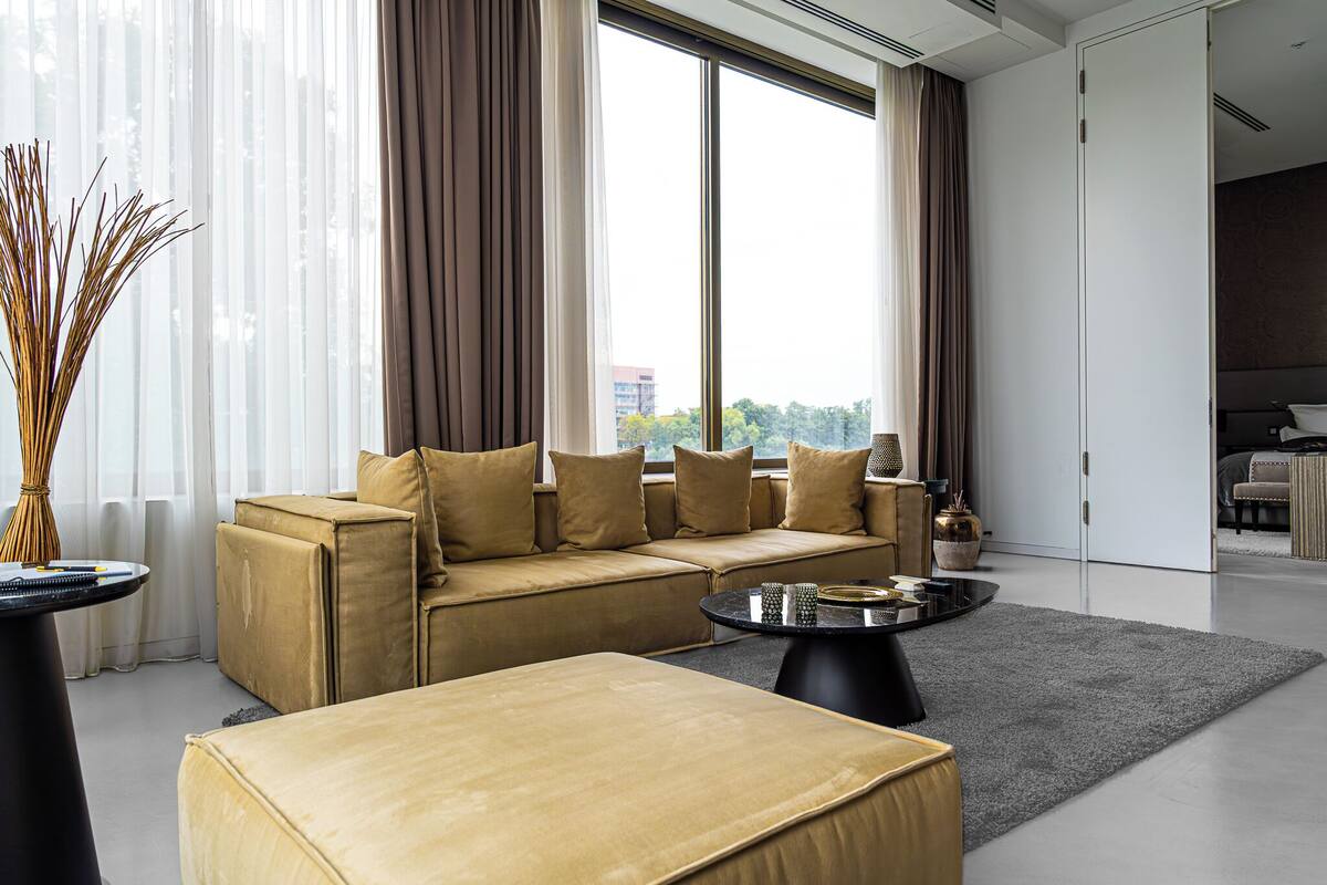 A modern living room with a beige sofa, a round coffee table, and a large window with curtains.