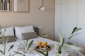 A neatly made bed with a tray of orange juice and croissants, a bedside table with a lamp, and a wall with abstract art.