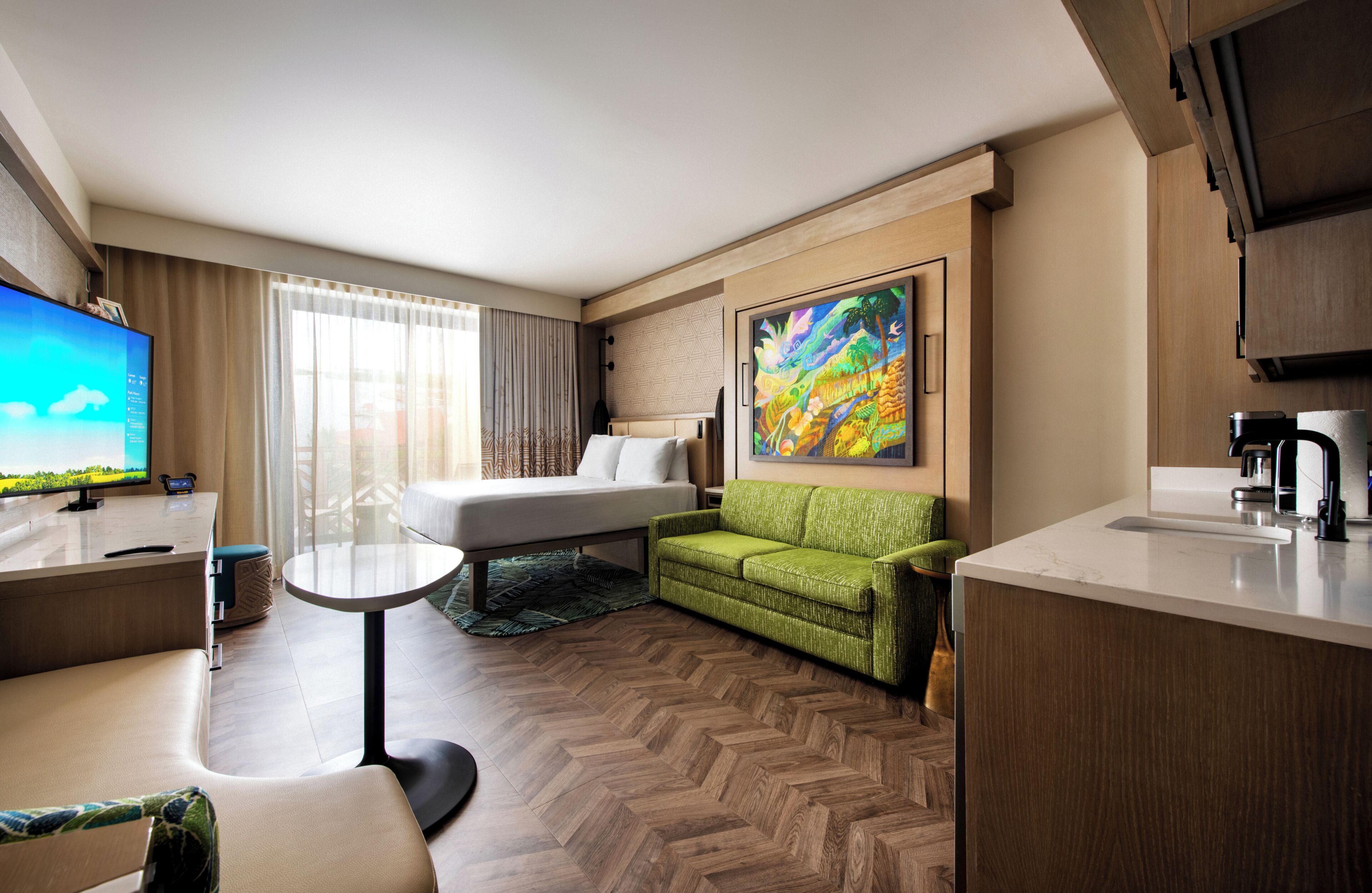 A hotel room with a bed, a green sofa, a small table, a TV, and a painting on the wall.