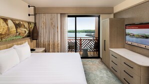 A hotel room with a bed, a TV, a desk, a chair, a balcony with a view of the water, and a painting on the wall. - Disney's Polynesian Villas & Bungalows (Lake Buena Vista)
