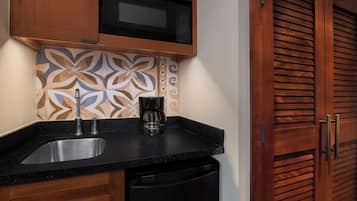 A kitchen with a black countertop, stainless steel sink, a coffee maker, and a microwave above the backsplash.