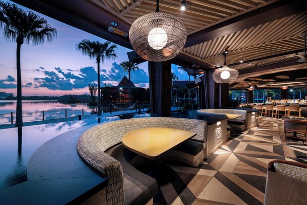 Un espacio con mesas y sillas al aire libre, con vista al agua y al atardecer.
