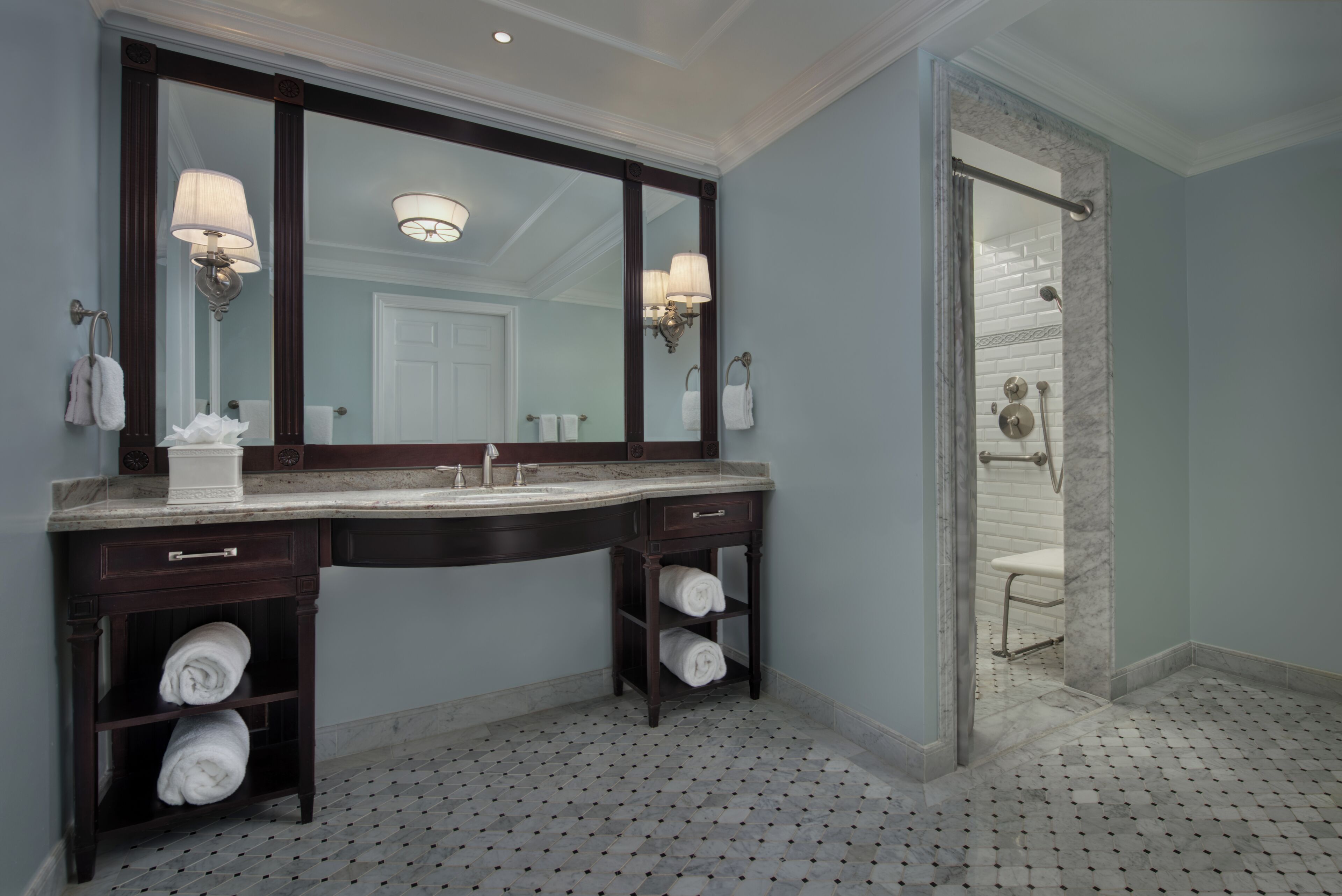 Een badkamer met een grote spiegel, twee wastafels, handdoekhouders en een douchehoek.